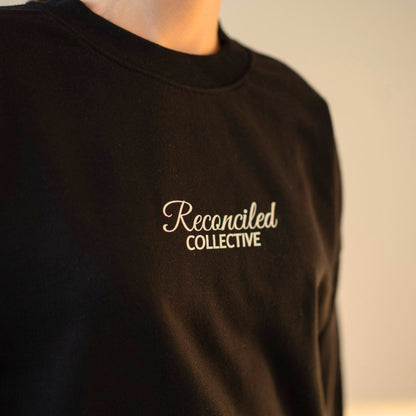 Black sweatshirt with 'Reconciled Collective' text on a plain background