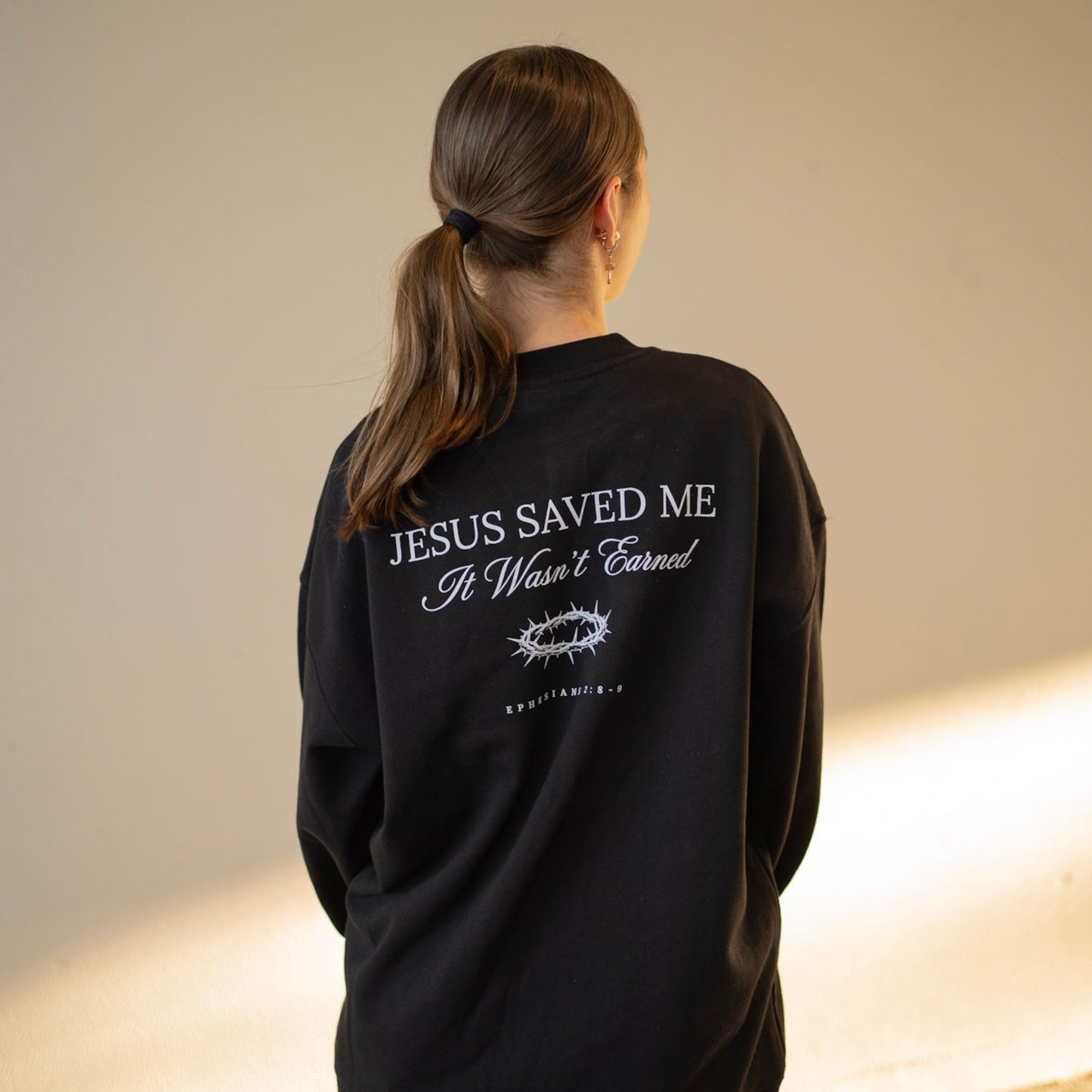 Person wearing a black sweatshirt with text on the back against a neutral background
