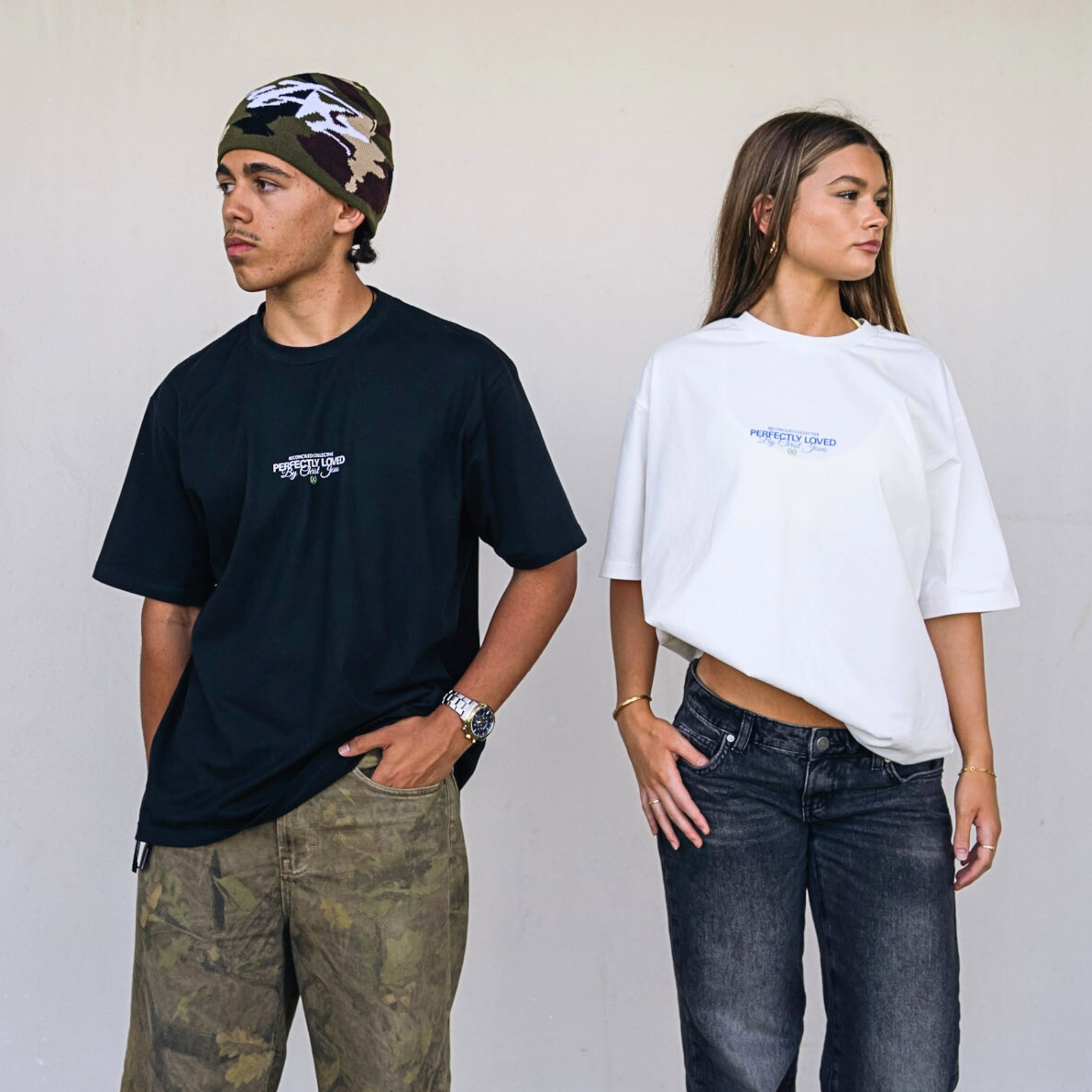 Male and female models wearing oversized Christian streetwear t-shirts in black and white featuring the “Perfectly Loved” design by Reconciled Collective, styled with relaxed urban fits.