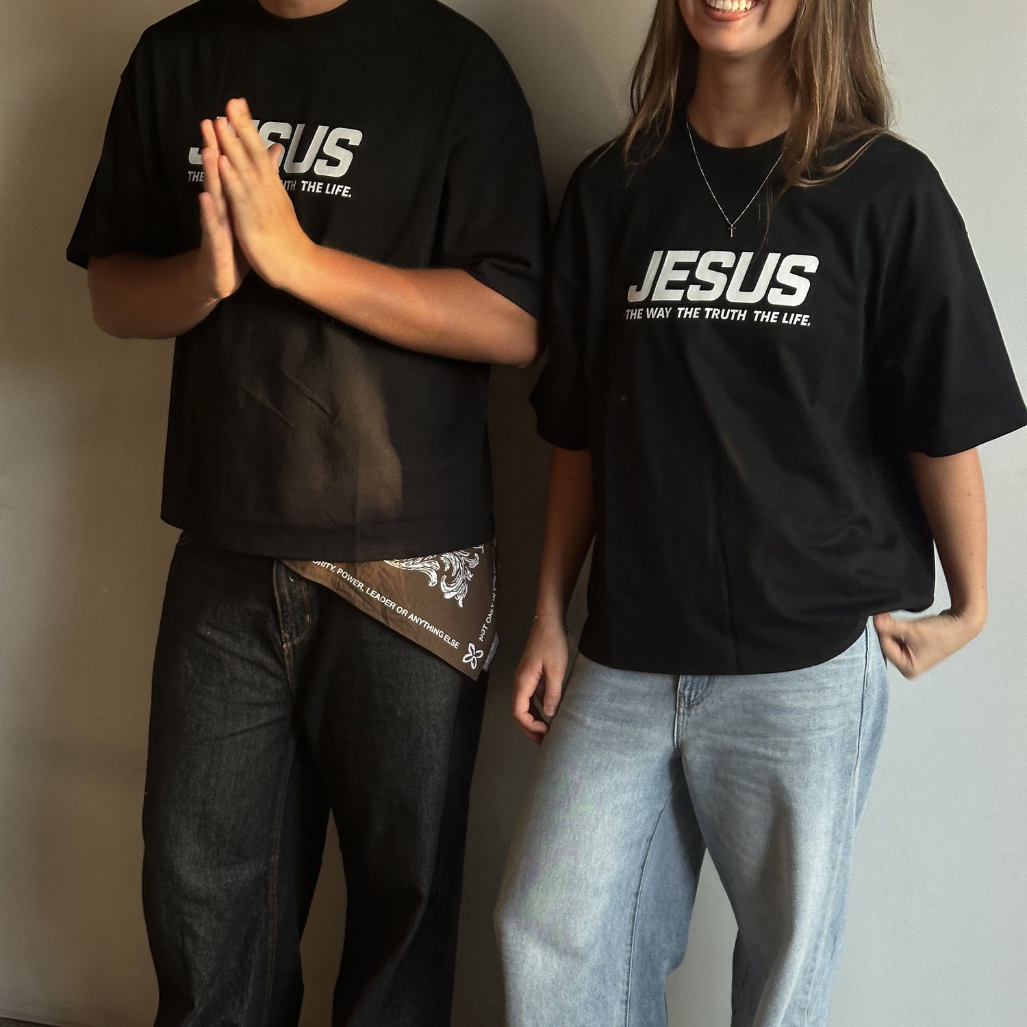 Two people wearing black t-shirts with 'JESUS' text, standing against a plain background.