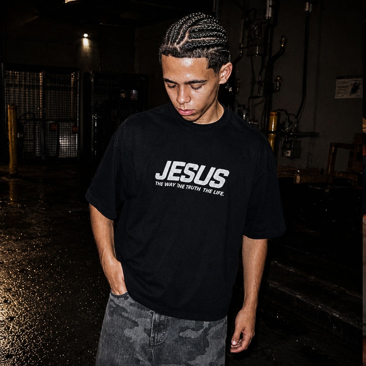 Person wearing a black t-shirt with 'JESUS' printed on it in a dark indoor setting.