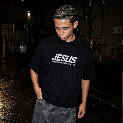Person wearing a black t-shirt with 'JESUS' printed on it in a dark indoor setting.