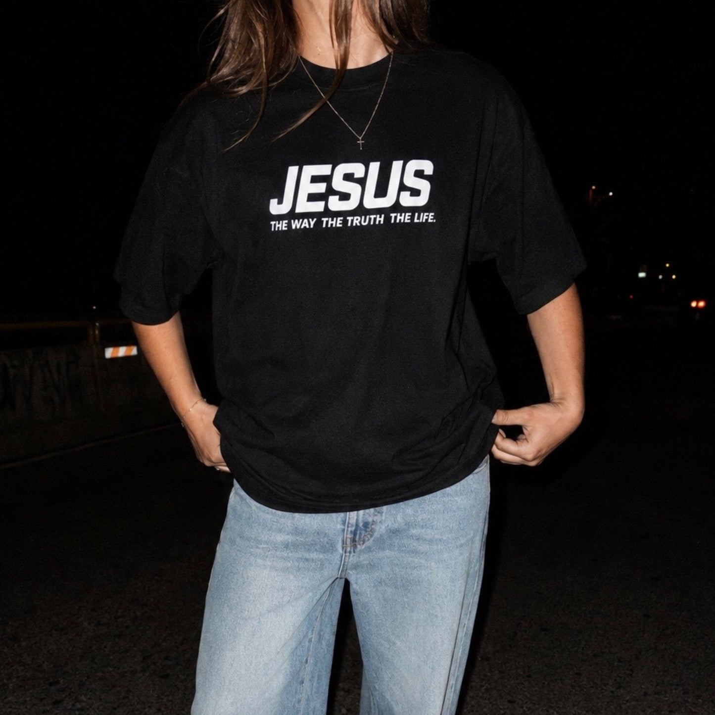 Person wearing a black t-shirt with 'JESUS THE WAY THE TRUTH THE LIFE' text at night.