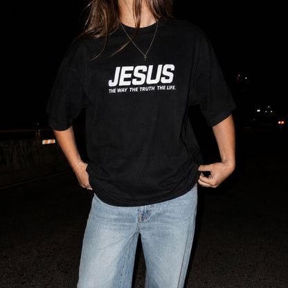Person wearing a black t-shirt with 'JESUS THE WAY THE TRUTH THE LIFE' text at night.