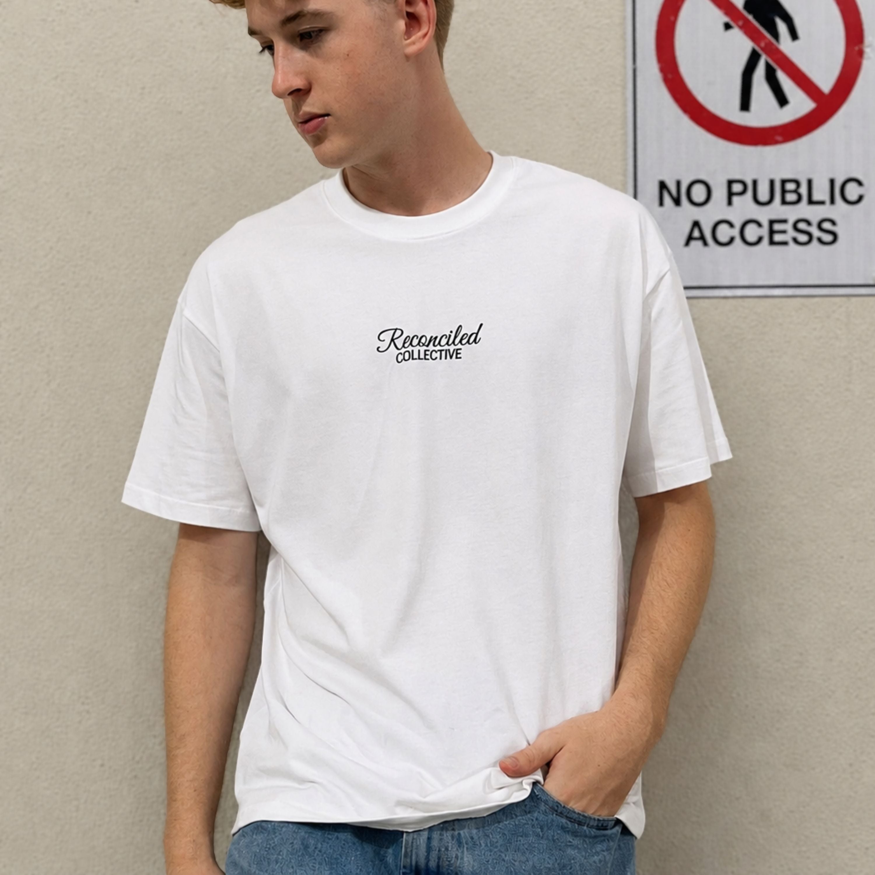 Person wearing a white t-shirt with text standing next to a 'No Public Access' sign.